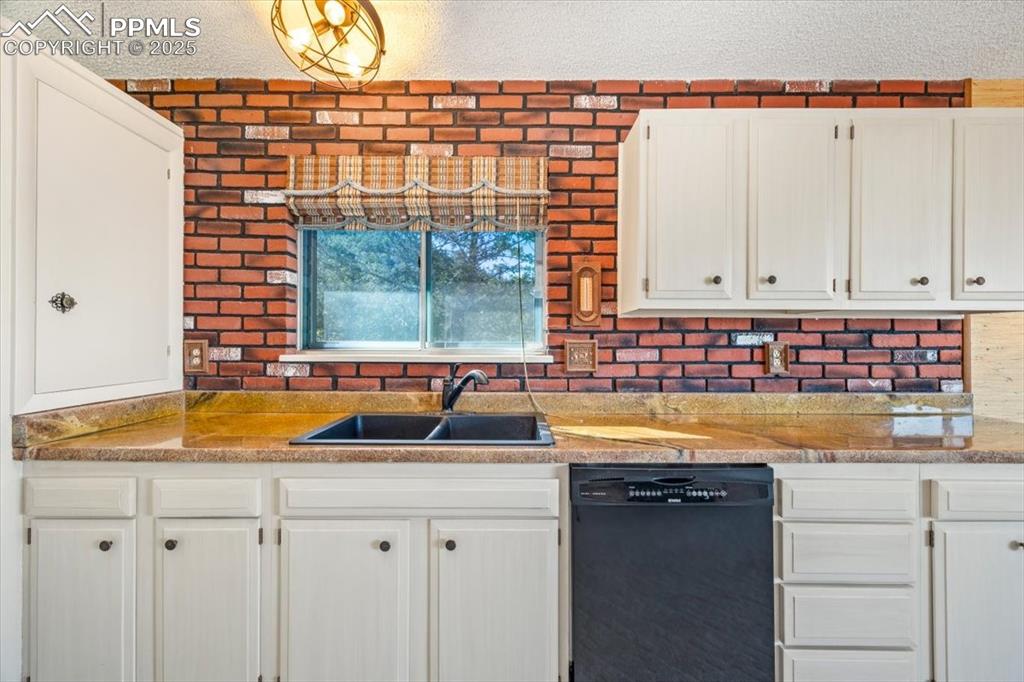 Kitchen with black dishwasher, a textured ceiling, white cabinets, and light stone countertops