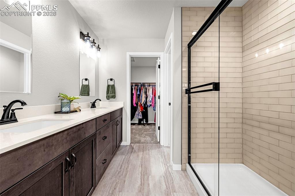 Primary bathroom with a beautiful walk-in shower, double vanity, a walk in closet, and luxury tile flooring 