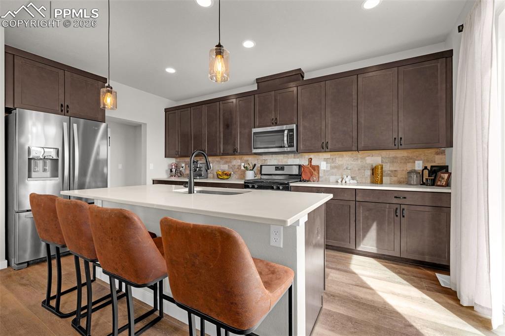 Kitchen featuring stainless steel appliances, dark espresso finished cabinetry, a center island, and luxury vinyl plank flooring