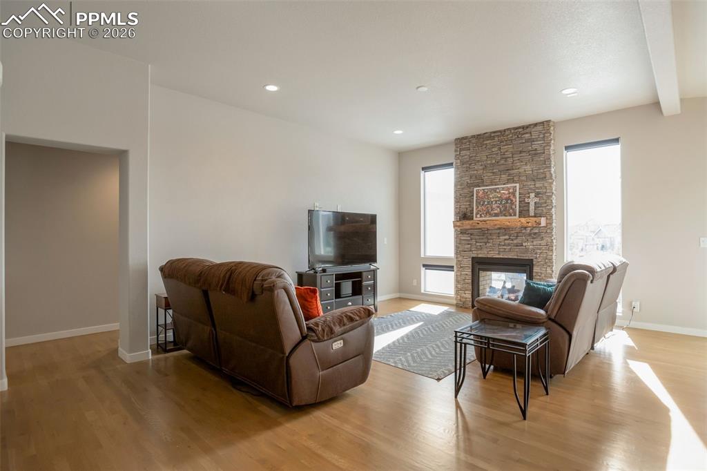 Living room featuring real white oak flooring, a stone indoor/outdoor double sided fireplace, recessed lighting, and high beamed ceiling
