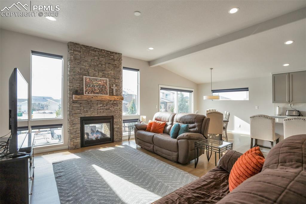 Living room featuring real white oak wood floors, a stone double sided indoor/outdoor fireplace, recessed lighting, and vaulted ceiling with beams