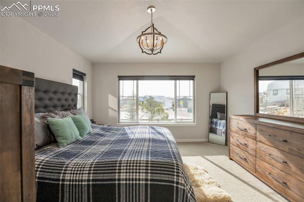 Primary Bedroom #1 featuring light colored carpet, a chandelier, and lofted ceiling
