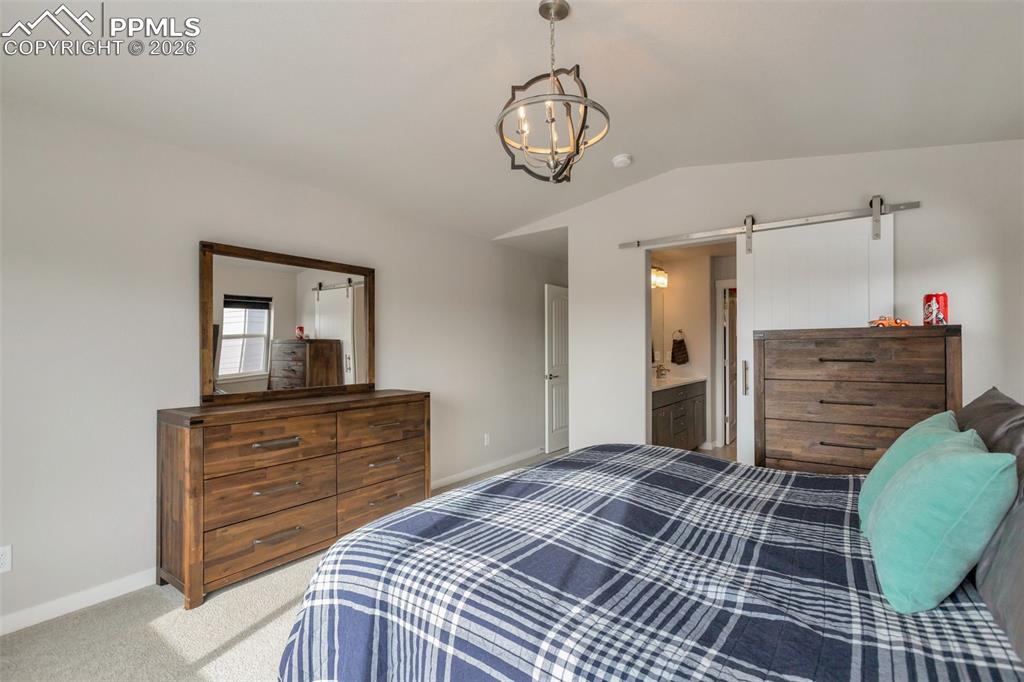Primary Bedroom #1 Main Level featuring a barn door, light colored carpet, lofted ceiling, suspended lighting, and en-suite bathroom