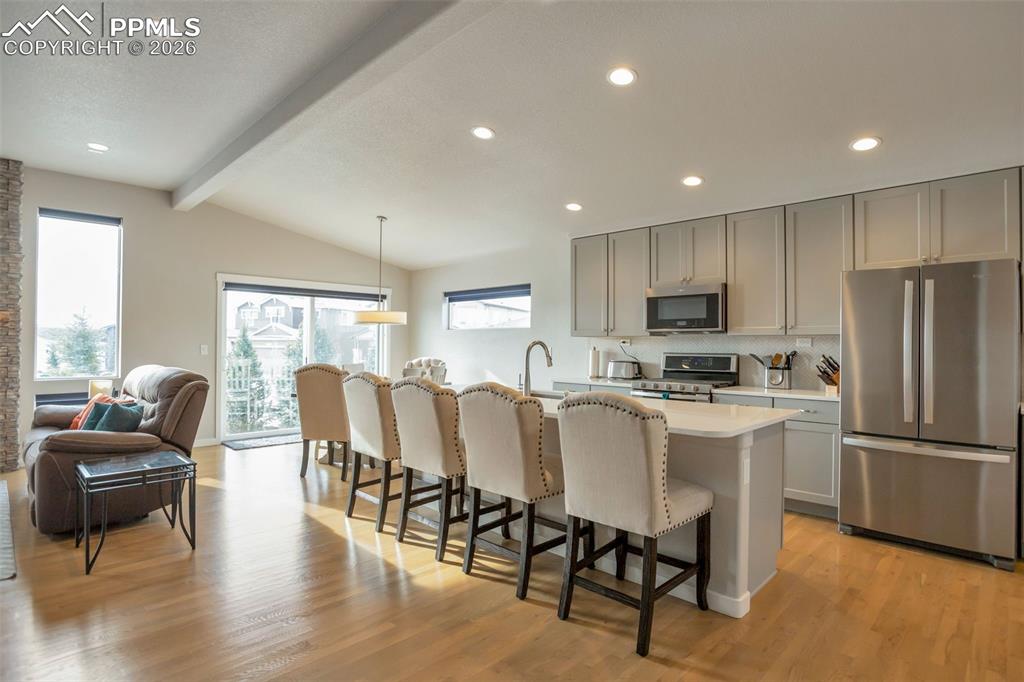 Kitchen with stainless steel appliances, a kitchen island with sink, a breakfast bar, lofted ceiling with beams, and real solid white oak floors
