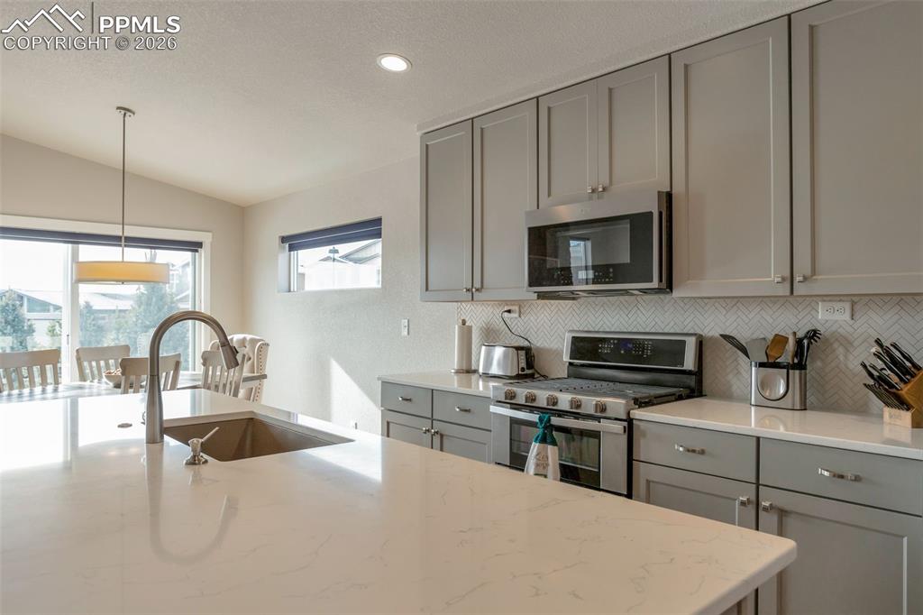 Kitchen featuring gray cabinetry, stainless steel appliances, quartz countertops and vaulted ceiling