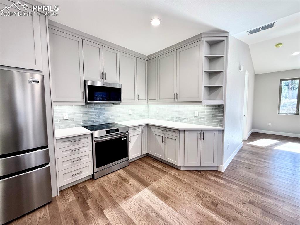 Full-sized Gourmet Kitchen with Quartz Countertops, Upper Cabinets to the Ceiling, Under-cabinet lighting., Induction Range, Included Stainless Still Fridge, and Wood Flooring.
