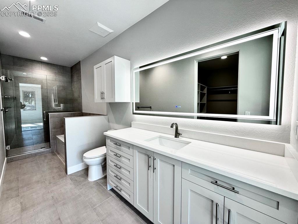Luxurious Primary Bathroom with Quartz Countertop, Deep Soaking Tub, Tiled Shower with Bench and Glass Door, and a Heated Mirror to avoid Fogging.