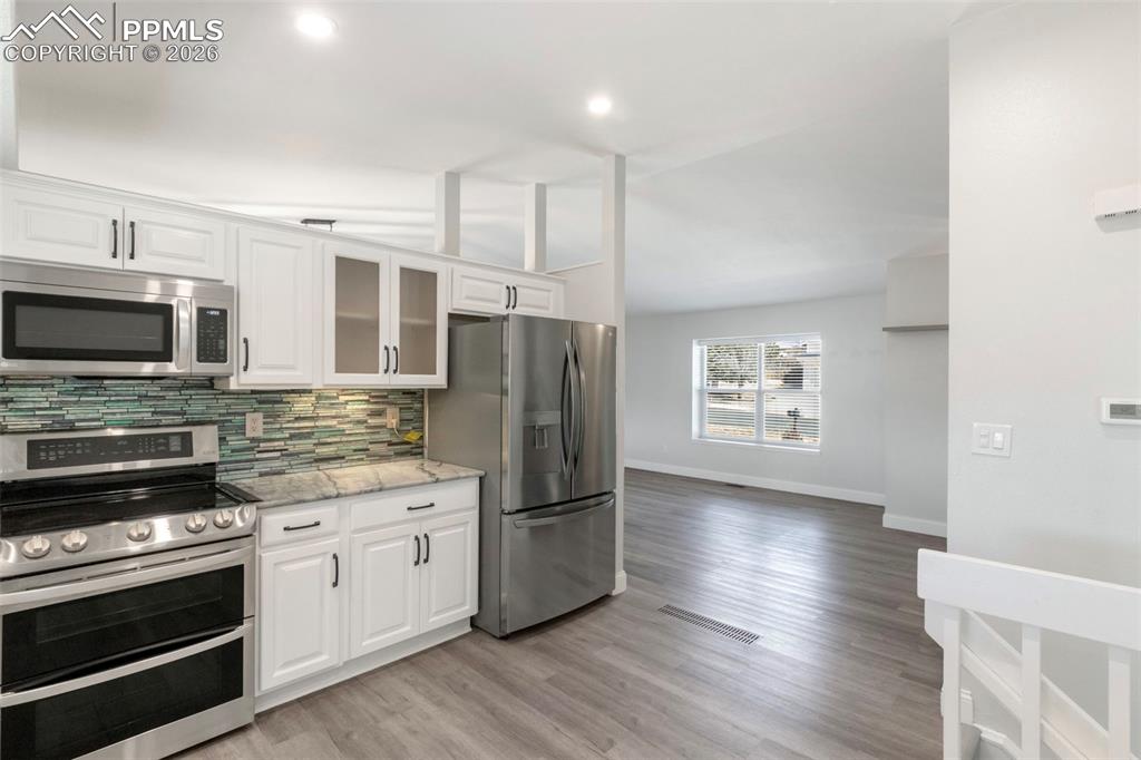 Additional view of Kitchen with stainless steel appliances, white cabinetry, light stone countertops, recessed lighting, light colored plank LVT flooring, and looking toward Formal Living Room with vaulted ceiling