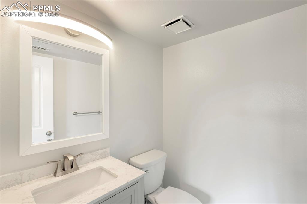 Half bath featuring vanity with solid surface countertop, toilet, attractive lighting, and LVT flooring