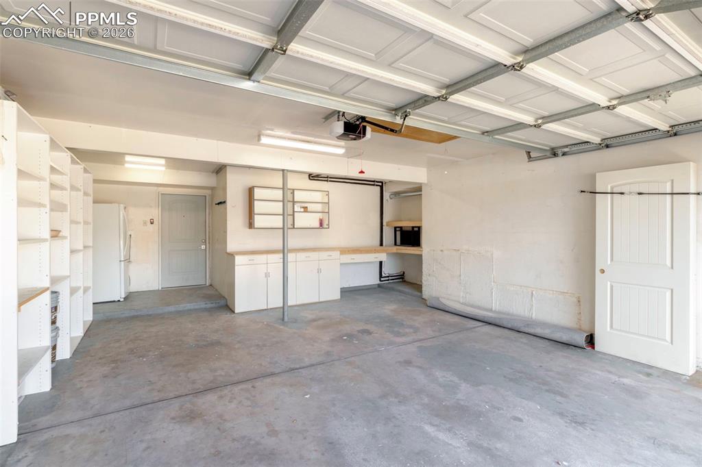 Oversized Garage featuring shelving, workshop area, overhead lighting, attic space, freestanding refrigerator and has direct access to the Family Room with a half bath on this level