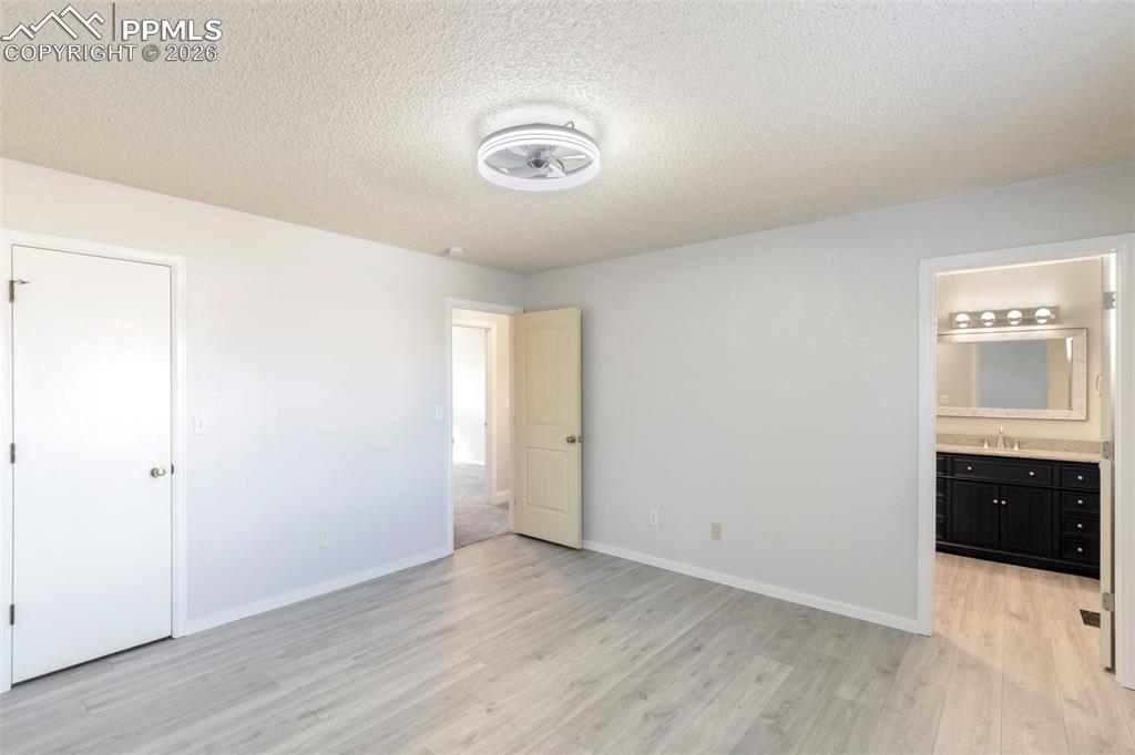 Primary bedroom featuring a walk-in closet, ceiling fan, ensuite bath, and light colored plank LVT floors