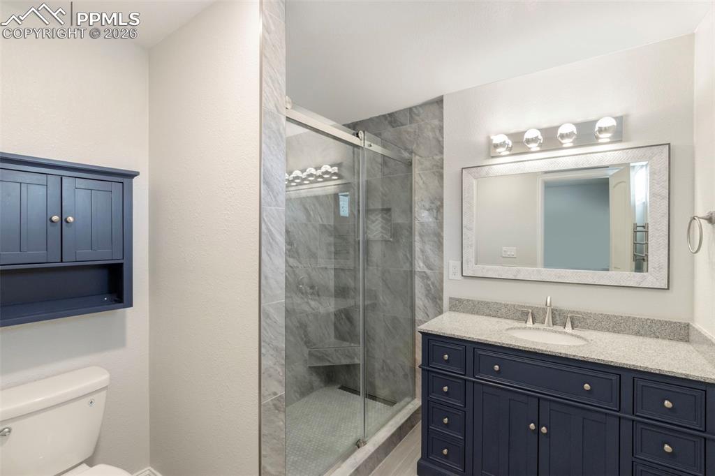 Updated Primary Bathroom features a free-standing, spa-like shower with floor to ceiling tile, linear drain, built-in niches, barn door style sliding glass doors; vanity with solid surface stone countertops and plenty of storage; attractive lighting and mirror; toilet with storage cabinet above; LVT flooring; and a window for natural light.