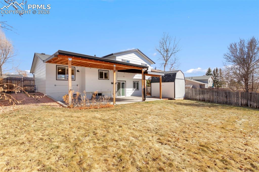 Back of property with a storage shed, a patio area, and a fenced backyard