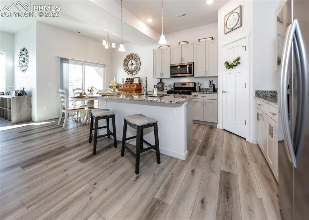 Kitchen with stainless steel appliances, light stone countertops, a center island with sink, a breakfast bar area, and light wood finished floors