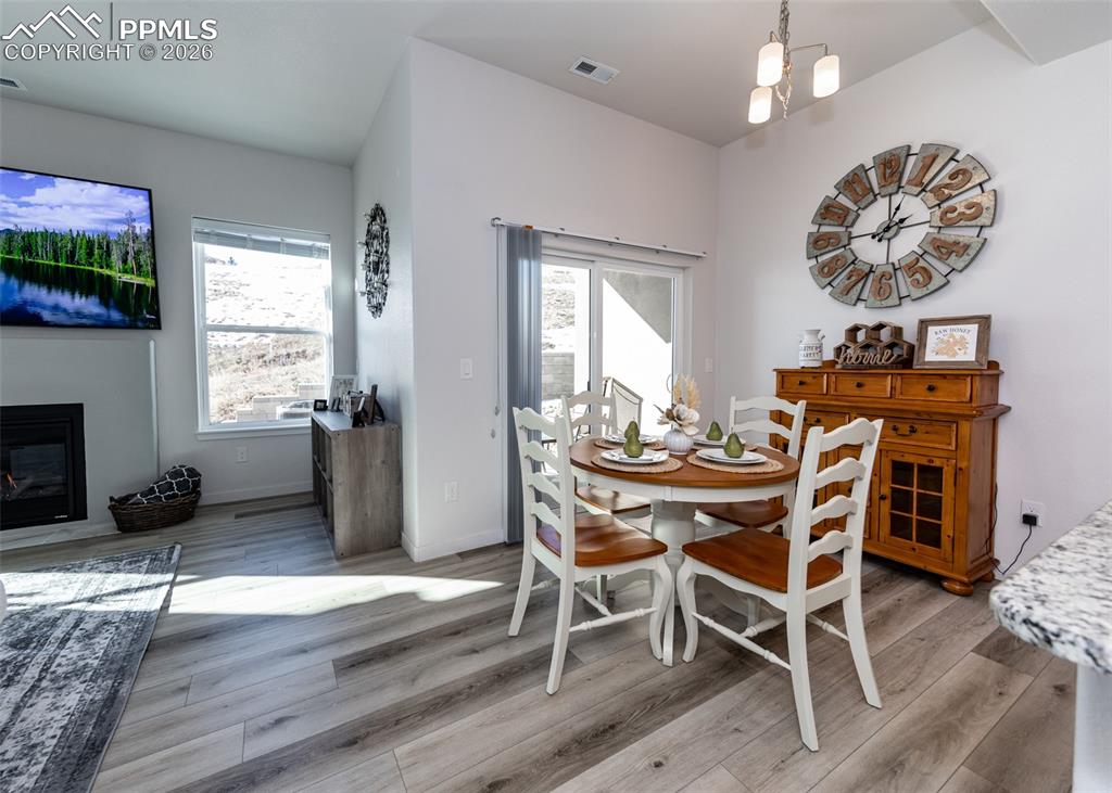 Dining area with light wood finished floors, hanging lights, and a glass covered fireplace