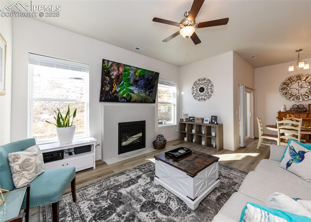 Living area with a ceiling fan, wood finished floors, and a fireplace with flush hearth