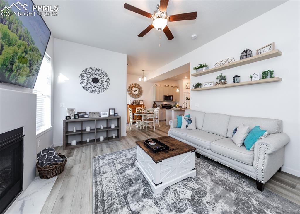Living room with a ceiling fan, a fireplace, and light wood finished floors