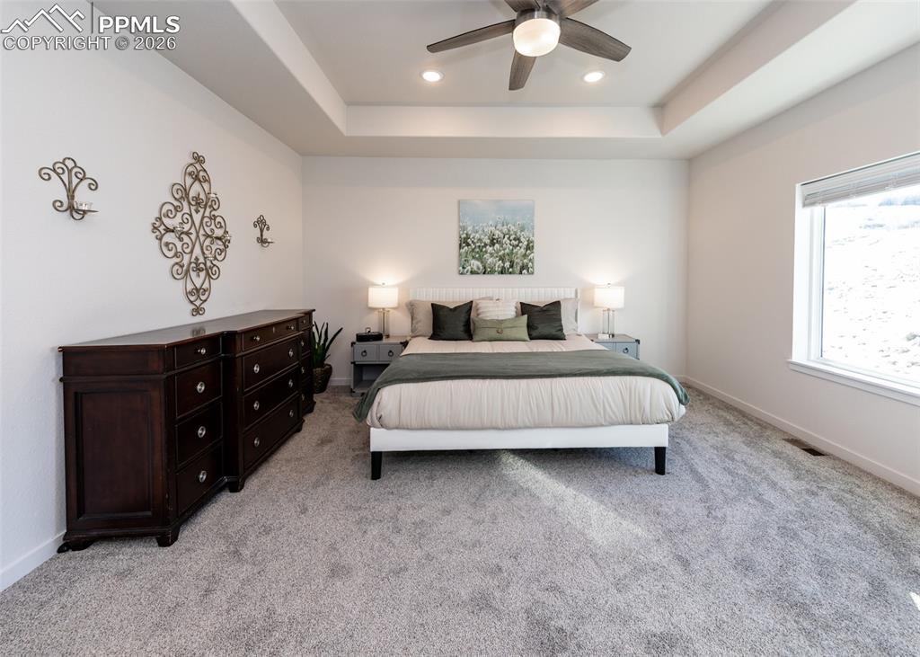 Bedroom with a raised ceiling, light carpet, ceiling fan, and recessed lighting