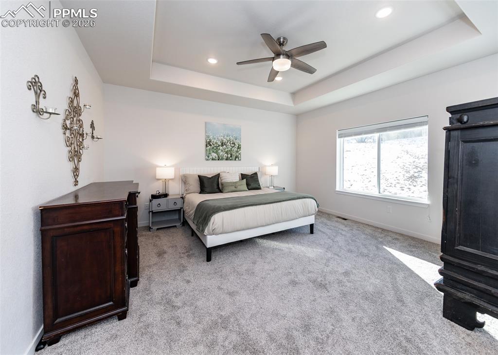 Bedroom with ceiling fan, light carpet, recessed lighting, and a tray ceiling