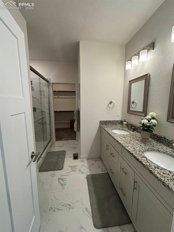 Bathroom with a spacious closet, double vanity, a shower stall, light marble finish flooring, and a textured ceiling