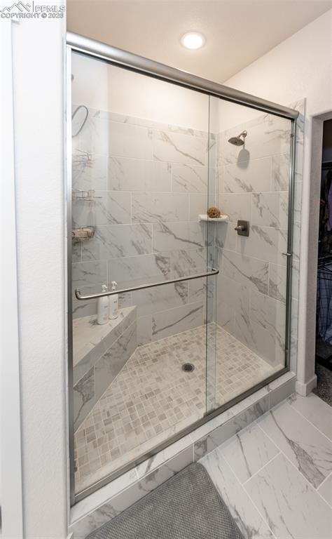 Full bath featuring light marble finish flooring, a shower stall, a spacious closet, and recessed lighting