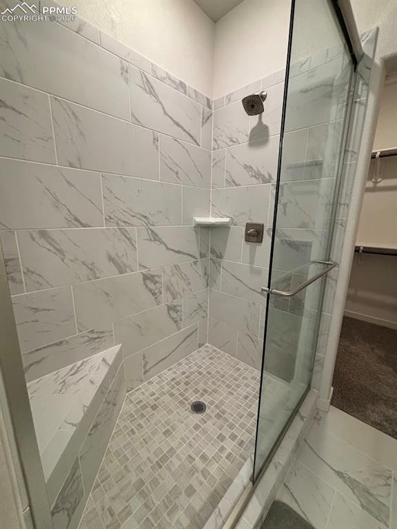 Full bath featuring a walk in closet, a shower stall, and marble look tile flooring