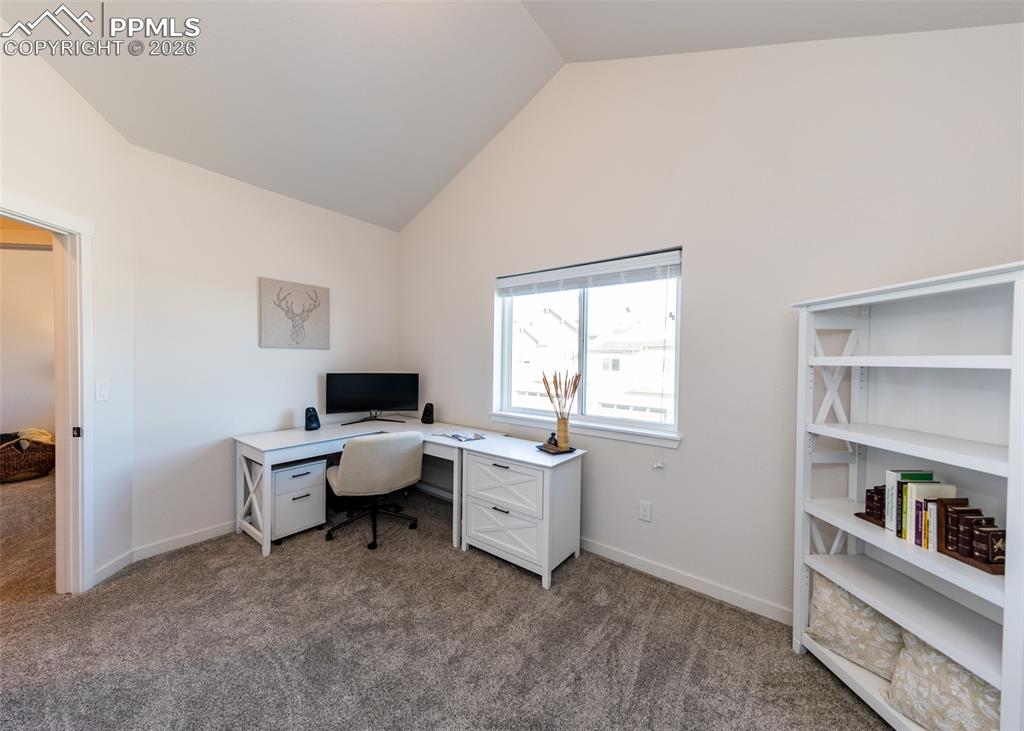 Office with dark carpet and lofted ceiling