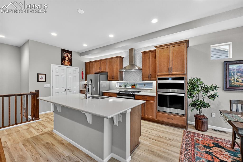 Kitchen with brown cabinetry, tasteful backsplash, appliances with stainless steel finishes, recessed lighting, and light wood-type flooring