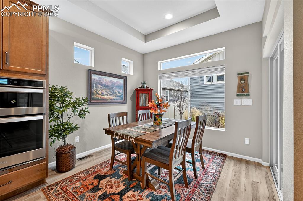 Dining area featuring light wood-style flooring, a tray ceiling, and healthy amount of natural light