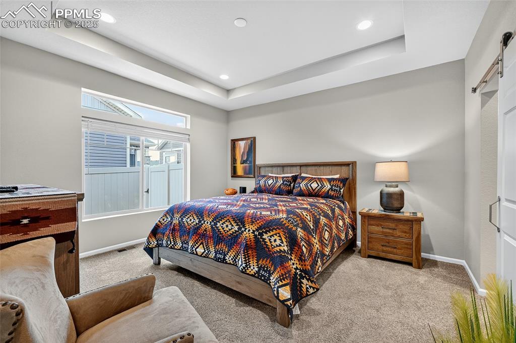 Bedroom featuring a raised ceiling, carpet, a barn door, and recessed lighting