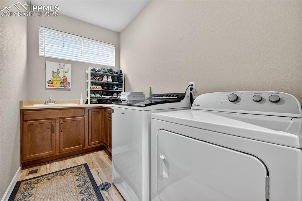 Washroom featuring a textured wall, washing machine and clothes dryer, light wood-style floors, and cabinet space