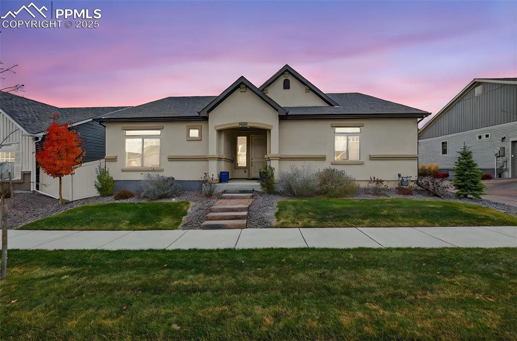 View of front of home with a yard, stucco siding, and a shingled roof