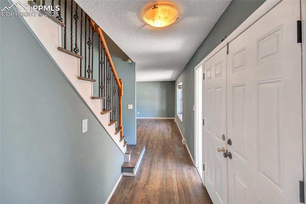 Entrance foyer with a textured ceiling, stairway, wood finished floors, and baseboards