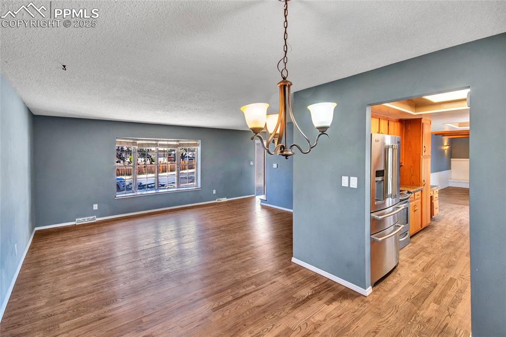 Unfurnished dining area with a textured ceiling, visible vents, light wood-style flooring, a notable chandelier, and baseboards