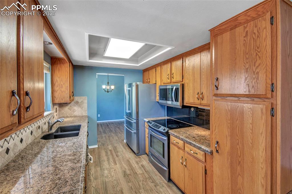 Kitchen featuring light wood finished floors, a sink, stainless steel appliances, a notable chandelier, and decorative backsplash