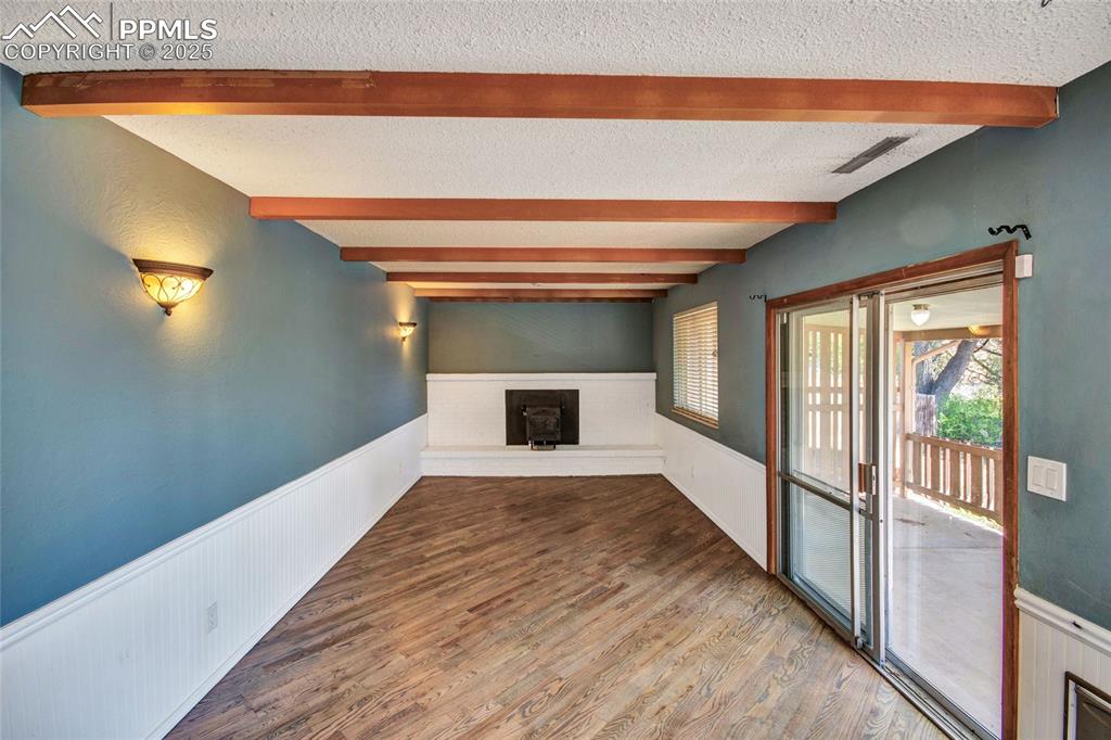 Unfurnished living room featuring wood finished floors, a wainscoted wall, beam ceiling, a textured ceiling, and visible vents