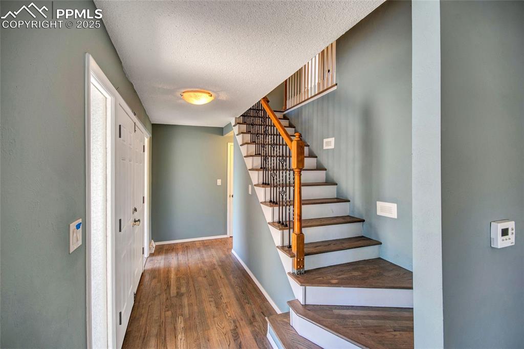 Foyer entrance featuring baseboards, stairs, a textured ceiling, and wood finished floors