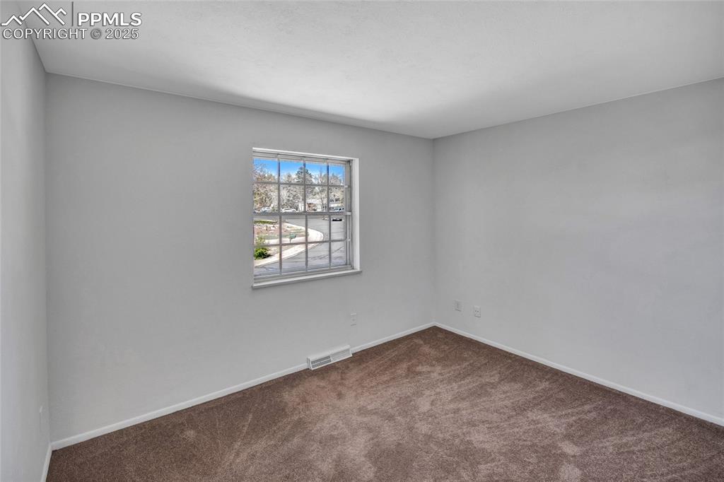 Spare room featuring dark colored carpet, baseboards, and visible vents