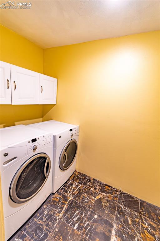 Washroom with marble finish floor, washing machine and dryer, and cabinet space