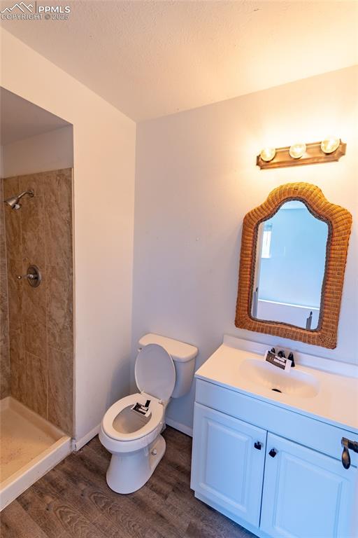 Full bath featuring vanity, toilet, tiled shower, and wood finished floors