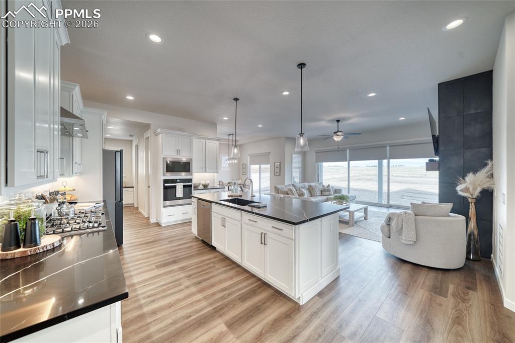 Kitchen with white cabinets, a kitchen island with sink, light wood finished floors, stainless steel appliances, and open floor plan
