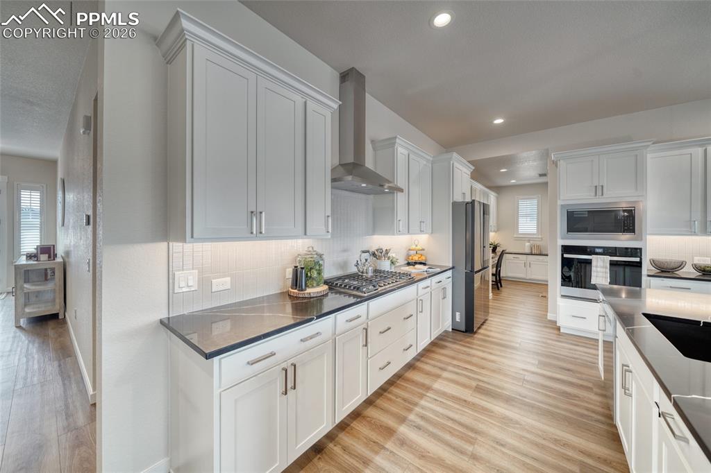 Kitchen featuring stainless steel appliances, light wood-style floors, white cabinets, backsplash, and dark stone countertops