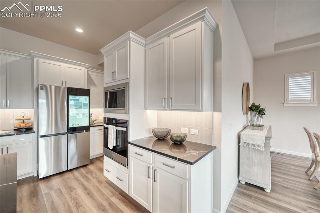 Kitchen with stainless steel appliances, light wood-style flooring, decorative backsplash, white cabinets, and recessed lighting