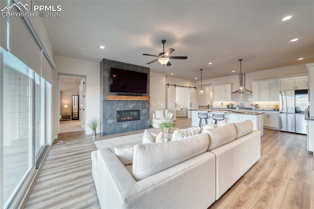 Living area with a barn door, ceiling fan, a tile fireplace, light wood-style floors, and recessed lighting