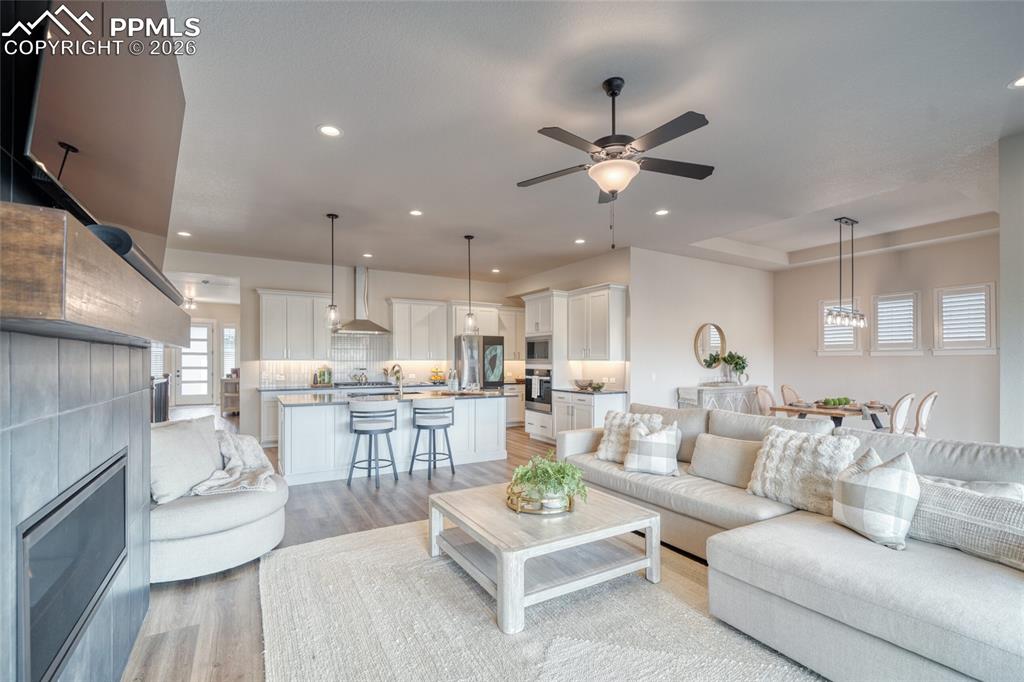 Living area featuring light wood-style floors, a tiled fireplace, a ceiling fan, and recessed lighting