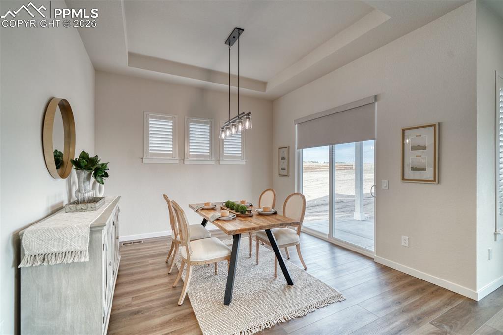 Dining area with healthy amount of natural light, a tray ceiling, and light wood-style floors
