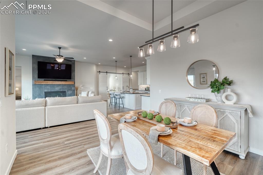 Dining space featuring a barn door, light wood-type flooring, a tiled fireplace, recessed lighting, and a ceiling fan