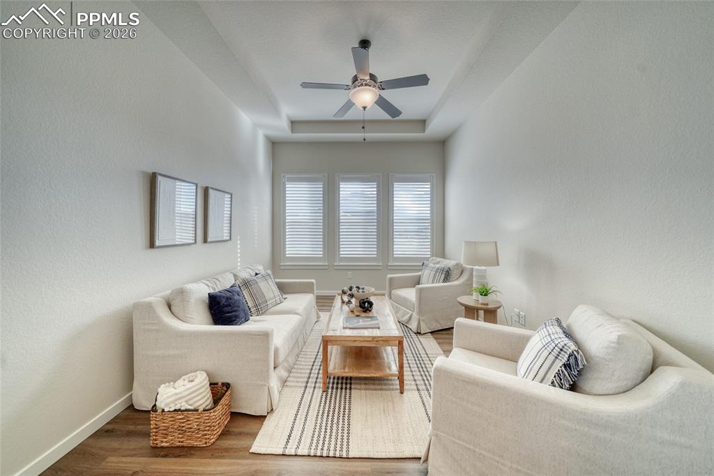 Living room with ceiling fan, wood finished floors, a textured wall, and a tray ceiling