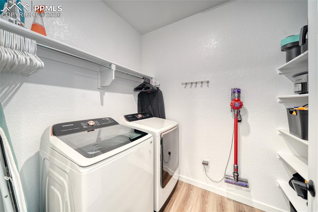 Laundry room featuring a textured wall, light wood-style floors, and washer and clothes dryer