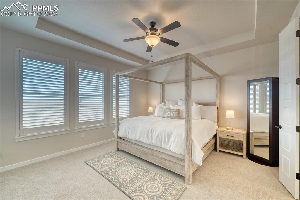 Bedroom with a tray ceiling, light colored carpet, and ceiling fan